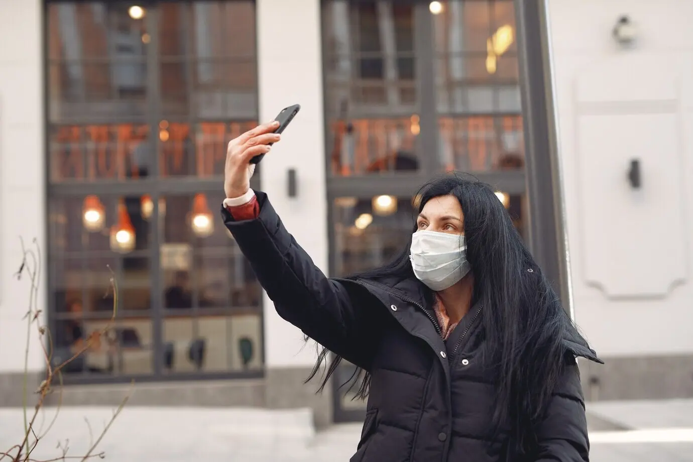 Mujer con mascarilla protectora sentada en la calle, haciéndose un selfie.