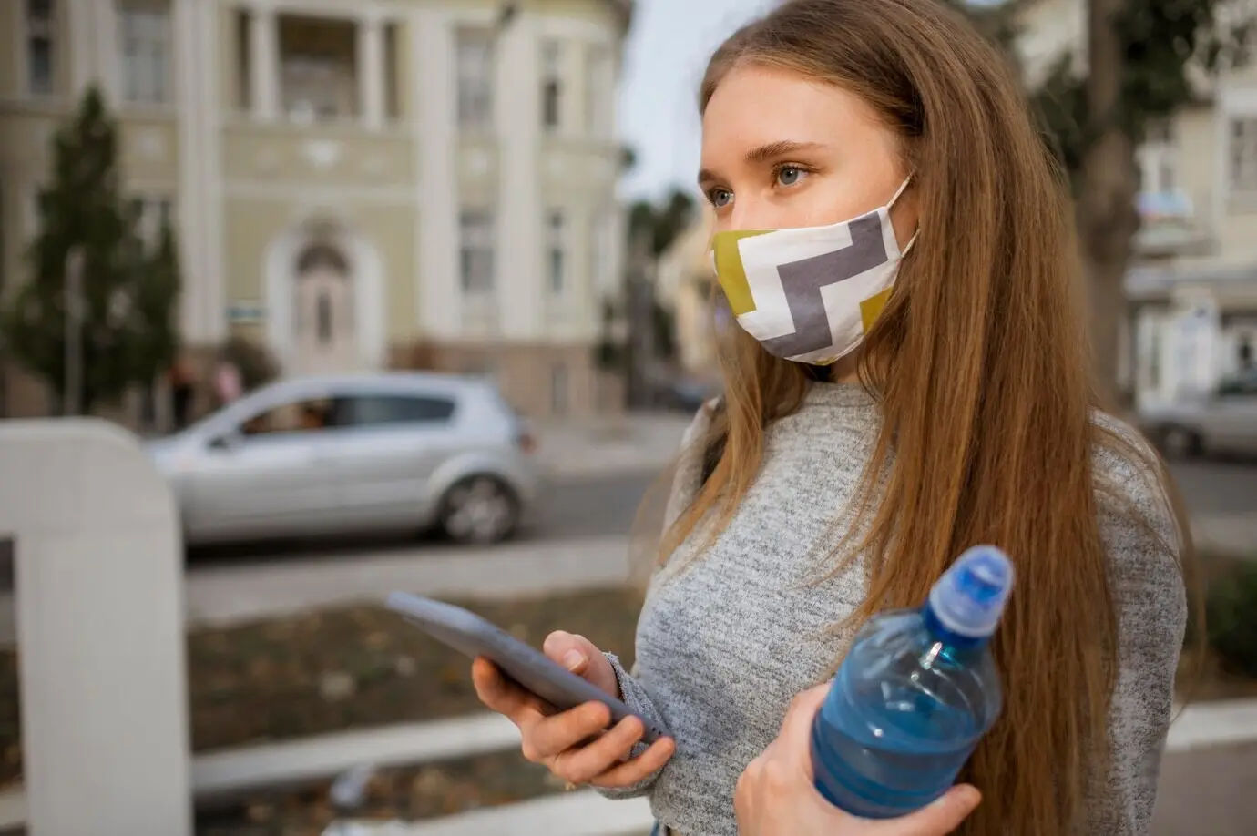 Vista lateral de una mujer con mascarilla médica que sostiene una botella de agua.